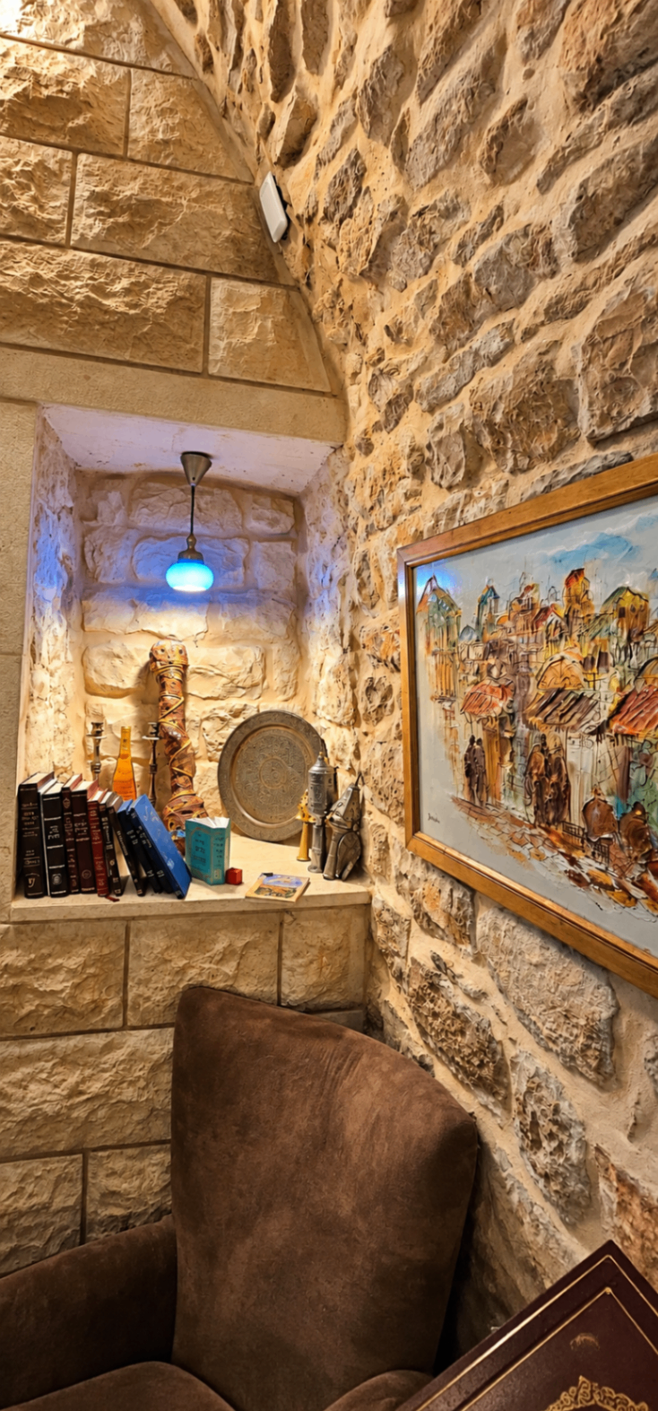 פינת קריאה בקיר האבן עם ספרים, חפצי אמנות וציור של רובע בצפת